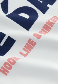 Bílá tkanina s námořnickomodrým a růžovým textem, který říká „HOOK LINE & SINKER.“ Materiál vypadá jemně a má mírně texturovaný povrch.