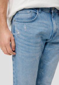 Jasnoniebieskie dżinsy o wąskim kroju, z przetarciami i pięcioma kieszeniami, ozdobione srebrnym guzikiem i nitami.