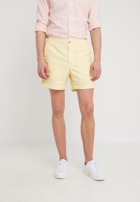 Žluté šortky s uvolněným střihem, vyrobené z lehkého materiálu. Mají zapínání na knoflík a postranní kapsy. Nosené s bílými teniskami.