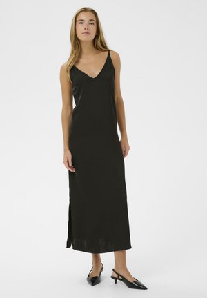 Žena v čiernych maxi šatách bez rukávov s výstrihom do V a bočným rozparkom, v kombinácii s čiernymi špicatými slingback lodičkami, na bielom pozadí.