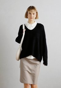 Un suéter de punto negro con un amplio escote en V, de corte holgado. Debajo, una camisa blanca con cuello. Combinado con una falda lápiz beige y un bolso ligero.