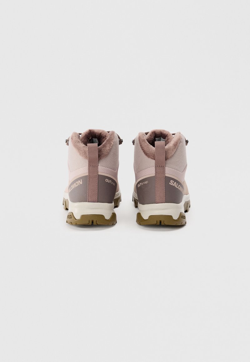 Chaussures de randonnée roses claires avec un extérieur texturé, un col rembourré et des accents marron. Équipées d'une semelle en caoutchouc solide pour une bonne adhérence.