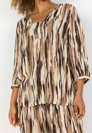 Vrouw draagt een beige, bruin en crème gestreepte lange mouwen top en bijpassende broek met losse pasvorm en V-halskraag.