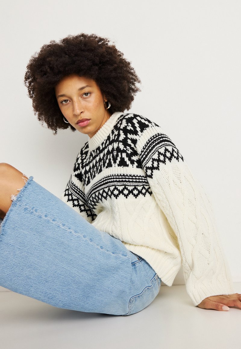 Kreemja ja musta värvi kampsun, millel on kootud soonik ja Fair Isle muster. Heledast sinisest teksaskostüümist seelik, millel on kulunud äär.