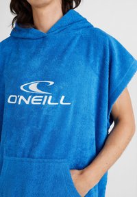 Zils frotēts pončo ar kapuci, ar priekšējo kabatu un baltu "O'Neill" logo. Mīksta tekstūra ar īsām piedurknēm.