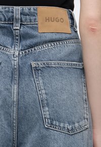 Πίσω όψη μπλε τζιν με λευκό δερμάτινο ταμπελάκι με την ένδειξη HUGO πάνω από την δεξιά πίσω τσέπη.