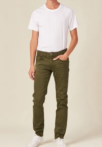 Jeans in misto cotone verde con vestibilità slim, design a cinque tasche e leggera scoloritura, abbinati a una t-shirt bianca a girocollo e sneakers bianche.