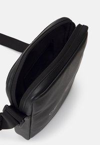 Borsa a spalla in pelle nera con una texture liscia, forma arrotondata e chiusura con zip. Presenta un design minimalista e una tracolla regolabile.