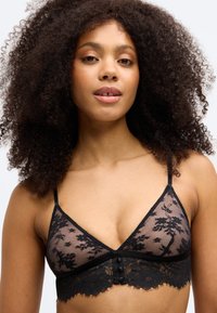 Črn čipkast bralette z rožnatim vzorcem, prosojnimi trikotnimi skodelicami, nastavljivimi naramnicami in čipkastim robom na dnu z gumbnimi detajli.