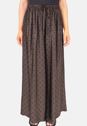 Braune Hose mit weitem Bein und dunkleren Polka-Punkten, elastischem Bund mit Kordelzug, getragen von einer Person, die mit entspannten Händen an den Seiten steht.