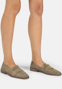 Suède instappers in taupe met een gestructureerde, geperforeerde bovenkant en strapdetails; platte houten hak; minimalistisch ontwerp.