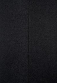 Czarna tkanina swetra o dzianinowej fakturze, z pionowym szwem na środku. Materiał wydaje się miękki i nieco elastyczny.