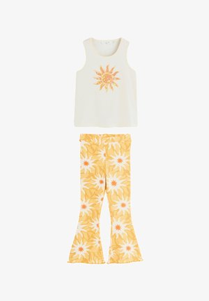 Haut blanc sans manches avec un motif soleil jaune, associé à un pantalon évasé jaune et blanc avec un motif soleil abstrait.