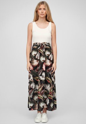 Jupe maxi avec un motif floral en noir, vert et rouge ; dotée d'une taille élastique et d'un détail noué ; associée à un débardeur blanc et à des baskets blanches.