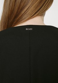 Svart kjole med et enkelt design, som har en synlig bakseam og en sølv "BOSS"-logo ved utringningen. Glatt stofftekstur.