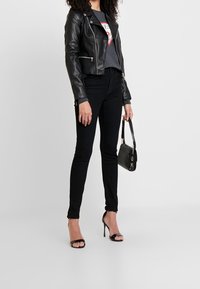 Chaqueta de cuero negra de biker sobre una camiseta gráfica gris, combinada con jeans skinny negros, tacones negros y un pequeño bolso negro.