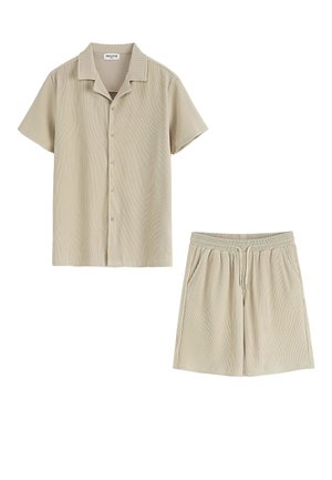 Chemise beige clair à manches courtes et shorts assortis, tous deux avec des rayures verticales et une texture douce. La chemise possède un col et une fermeture à boutons.