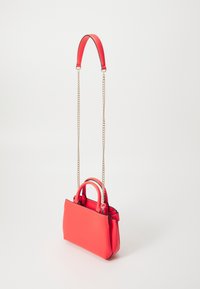 Red handbag with short handles and a long gold chain strap, displayed against a plain white background.