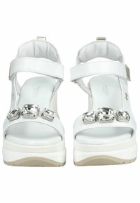 Sandali platform bianchi con una finitura lucida e texture, dotati di tre grandi gemme trasparenti sulla fascia anteriore e cinturini alla caviglia regolabili.