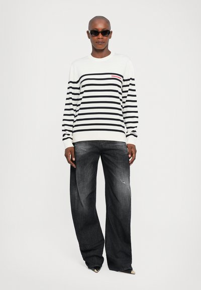 Striped knit sweater in black and white, featuring long sleeves and a crew neckline. Paired with wide-leg dark denim jeans with distressed details.