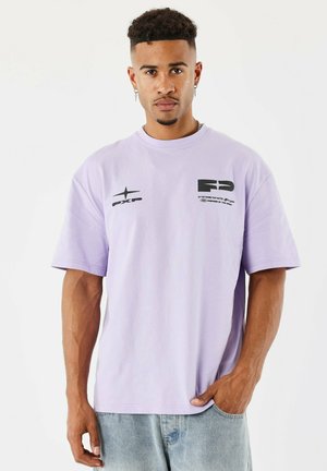 Camiseta de manga corta lavanda hecha de tela suave, con acentos de logo negro en el pecho y en la parte superior izquierda. Ajuste regular y diseño de cuello redondo.