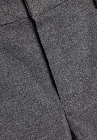 Tissu gris avec une finition texturée, présentant des plis plats et des détails de couture subtils. Le matériau semble doux et structuré.