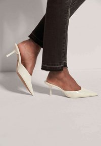 Witte gepatenteerde leren muiltjes met een spitse neus en een slanke stilettohak, met een gladde textuur en een open achterontwerp.