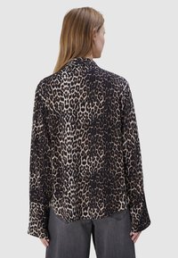 Lijnshirt met luipaardprint in een zachte, lichte stof met een losse pasvorm, met een zwarte achtergrond en tan vlekken. Lange mouwen met een ontspannen kraag.