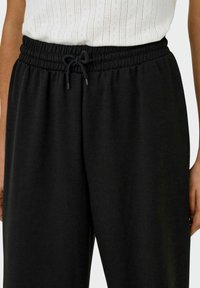Schwarze Sweatpants mit elastischem Bund und verstellbarem Kordelzug. Weicher, glatter Stoff mit lockerer Passform und minimalen Nähdetails.