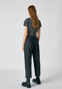 Haut court noir à motif floral associé à un jean en denim gris taille haute et fuselé. Le mannequin porte des bottes en caoutchouc noires épaisses.