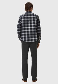 Camicia flanella a quadri da uomo in bianco e nero con maniche lunghe, orlo curvo e vestibilità comoda, abbinata a pantaloni e scarpe scure.