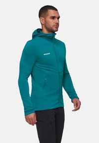 Teal hoodie met een rits sluiting, gemaakt van gladde, rekbare stof. Bevat zijzakken en een wit logo op de borst.