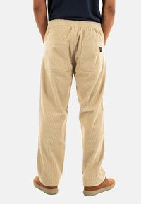 Beige corduroy broek met een relaxte pasvorm, elastische tailleband en twee achterzakken. De stof heeft een ribbeltextuur en zichtbare stiksels.