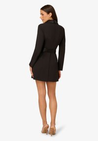 Robe noire ajustée à manches longues, taille ceinturée et col structuré. Tissu lisse avec une silhouette ajustée, longueur au-dessus du genou.