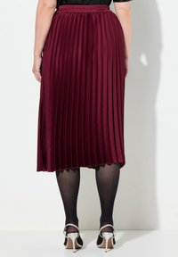 Burgundy plisserad midikjol med elastisk midja, slät textur och en fåll som når strax under knäna. I kombination med klackskor.