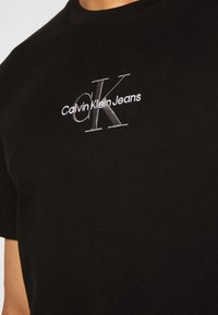 Czarna bawełniana koszulka z krótkim rękawem, z haftowanym srebrnym logo "Calvin Klein Jeans" i "CK" z przodu. Okrągły dekolt.