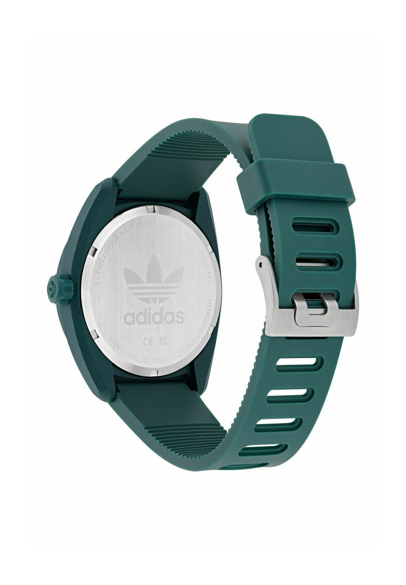 Reloj con correa de silicona verde y caja redonda de acero inoxidable. Presenta una correa texturizada y un fondo plateado con un logotipo grabado.
