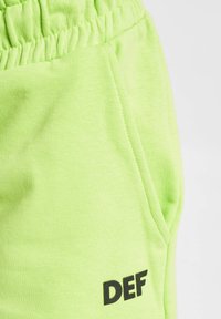 Neongrüne Baumwoll-Sweatpants mit einem elastischen Bund und einer Seitentasche, mit einem schwarz gedruckten "DEF"-Logo auf dem linken Bein.