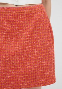Jupe mini tissée en rose et orange vif, avec un motif texturé. Elle dispose d'une taille élastique et de poches latérales.
