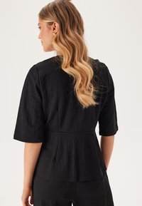 Svart peplumtröja med korta ärmar, som har ett texturerat tyg och ett åtsittande midja för en skräddarsydd look.