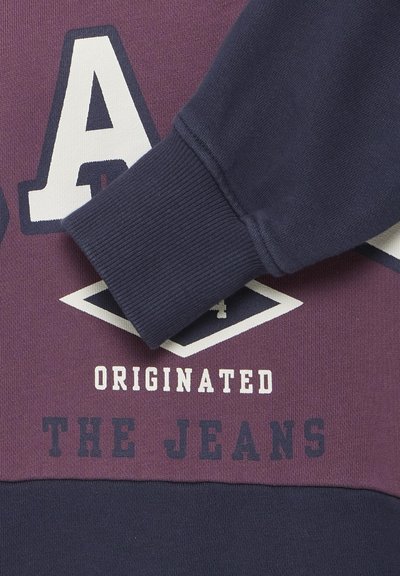 Hanorac violet și marină cu literă albă și modele geometrice, având o textură în rib cu manșete. Detalii de brand proeminente vizibile.