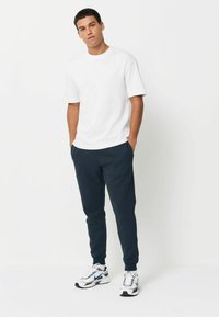 Balta īsā piedurkne krekls, tumši zili sporta bikses un baltas sporta kurpes ar melniem un ziliem akcentiem. Tīras līnijas un brīva piegriezuma.