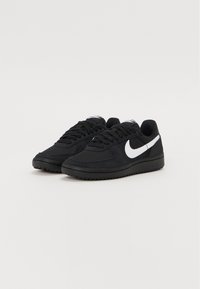 Sorte sneakers med en tekstureret stofoverdel, der har et hvidt Nike-swoosh, rund tå og flad gummisål. Snørebåndsdesign.