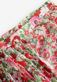 Tissu à motifs floraux avec des plis, présentant de grandes fleurs rouges et roses sur un fond clair. Le matériau semble léger et fluide.