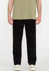 Black corduroy pants with a straight cut, textured fabric, and two side pockets, paired with a green t-shirt and white sneakers.