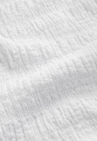 Tissu blanc texturé avec un motif froissé, présentant des crêtes inégales et une apparence douce et légère.