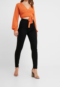 Top corto naranja con canalé y mangas largas, atado a la cintura, combinado con pantalones skinny negros y sandalias de tacón cuadrado con estampado de serpiente.