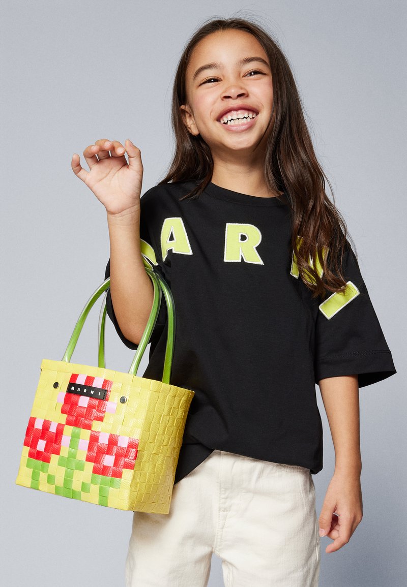 Saco de mão amarelo trançado com padrão quadriculado em vermelho e verde, apresentando duas alças verdes e um rótulo preto com a inscrição "HARNI."