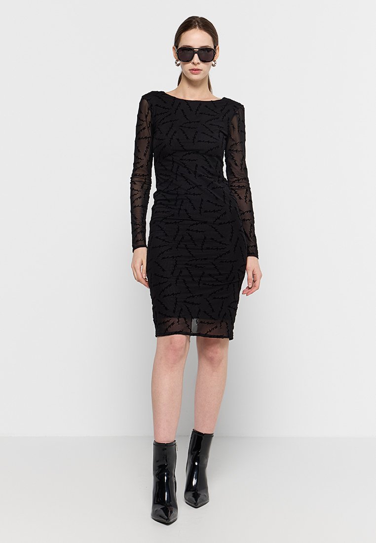 Vestido negro ajustado con mangas largas de tul, patrón texturizado y escote redondo. Combinado con botas de tobillo negras brillantes y gafas de sol.
