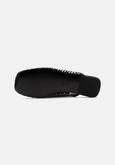 Semelle plate noire de chaussure avec un talon carré, montrant une prise texturée et une partie d'une tige noire et argentée à motif.